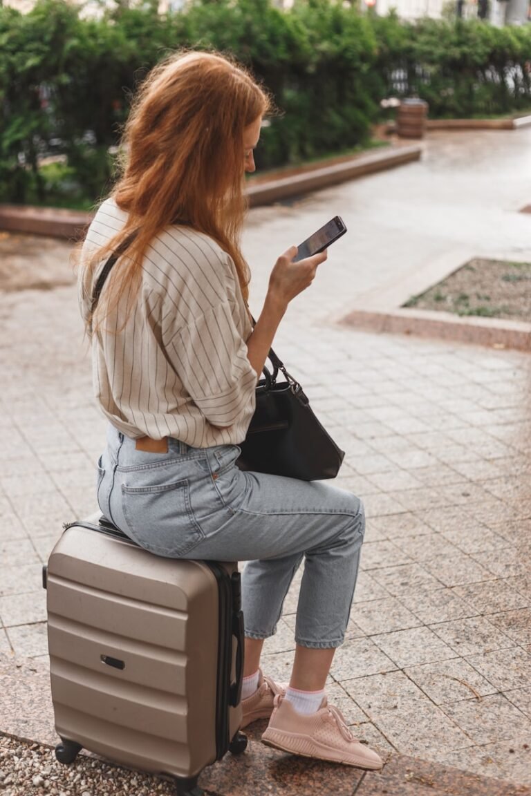 woman in white long sleeve shirt and blue denim jeans sitting on white and black luggage